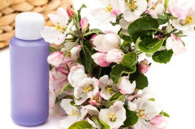 Hasır sepetin yanında beyaz arka planda armut çiçekleri olan leylak kozmetik şişesi. Doğal organik kozmetik konsepti