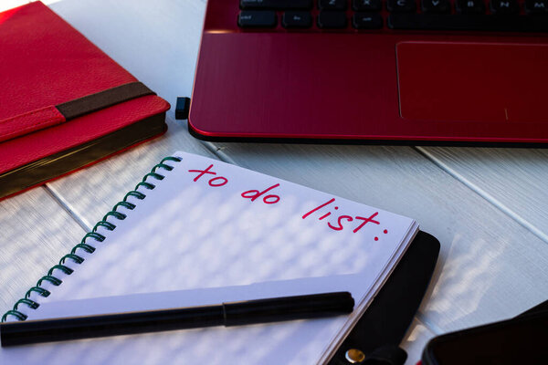 Notebook with To Do List with phone, red diary and laptop on a white wooden background