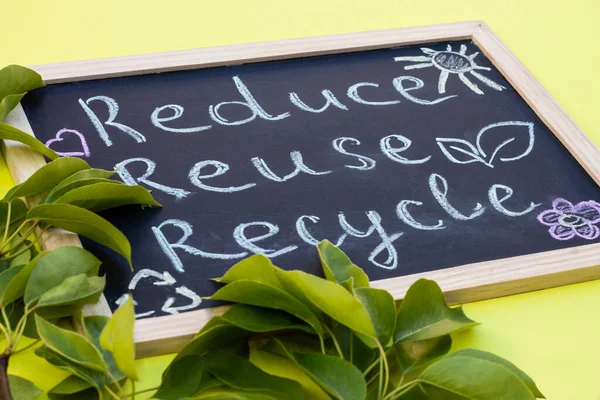 Chalk board Reduse Reuse Recycle sign on a yellow background with green leaves