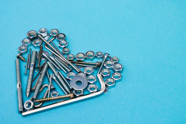 Heart laid out of bolts, nuts, wrenches and other construction tools on a blue background. Father\'s day concept. Copyspace
