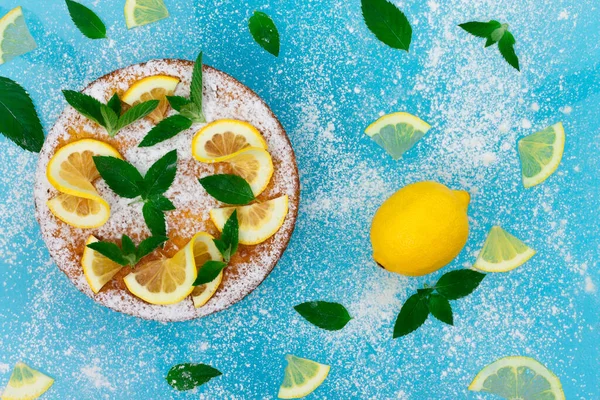 Lemon pie with lemon slices, mint and powdered sugar on a blue background. Top view, copy space.