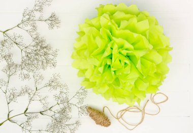 Beyaz ahşap masa arkaplanındaki kağıt mendilden açık yeşil pofuduk ponpon. Üst görünüm.