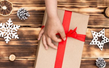 Noel 'de ve yılbaşında kırmızı kurdeleli el sanatları kağıdında hediye veren ya da alan eller. Üst görünüm.