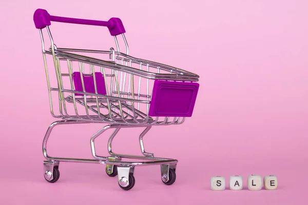 Shopping cart with letters SALE on a pink background, copy space.