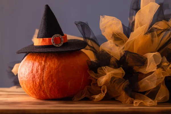 Halloween orange pumpkin in a witch hat on a blue background with black and orange tulle, copy space.