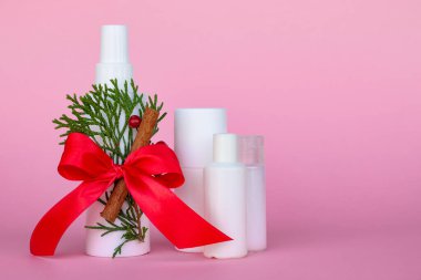 Parlak kırmızı kurdeleli kozmetik şişeleri, kırmızı böğürtlen, Noel ağacı dalı ve pembe arka planda tarçın çubuğu. Boşluğu kopyala.