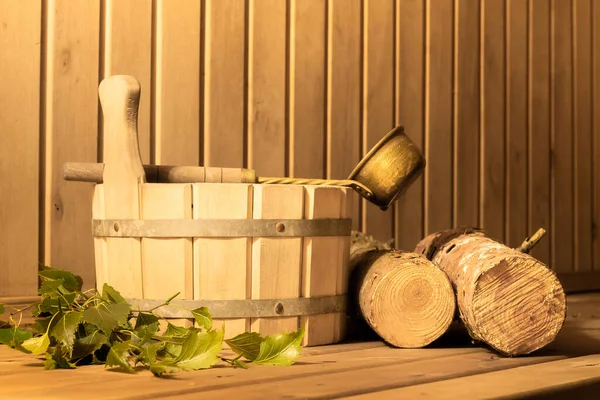 Wooden bucket, birch broom, firewood and ladle in the steam room of the sauna, copyspace