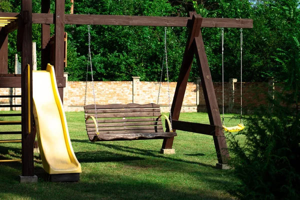 民家の中庭にあるレンガ造りの柵を背景に スイング スライド 階段のある木製の遊び場 — ストック写真