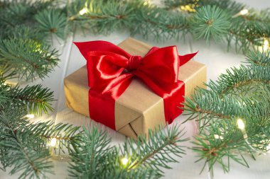 El işi kağıdına sarılı bir hediye ve beyaz ahşap arka planda LED lambaları olan yeşil dallı kırmızı kurdele. Mutlu Noeller ve mutlu yıllar konsepti