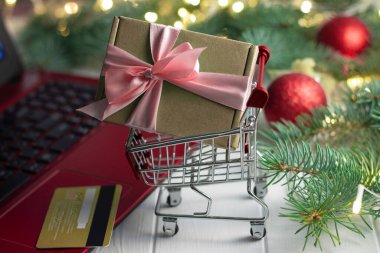 Laptop klavyesi, kredi kartı, ampulleri ve beyaz arka planda parlak topları olan bir Noel ağacının dalları yanında hediyeli bir tramvay. Noel ve Yeni Yıl çevrimiçi alışveriş kavramı