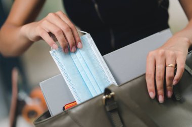 Bir otobüs durağında el çantasından maske çıkarırken elini kapat.