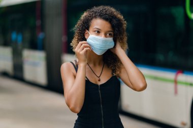 Otobüs durağında yüz maskesini Coronavirus 'a karşı ayarlayan genç bir kadın.