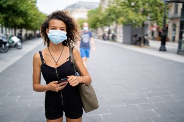 Koronavirüsten korumak için maske takan genç bir kadın sokakta yürüyor.