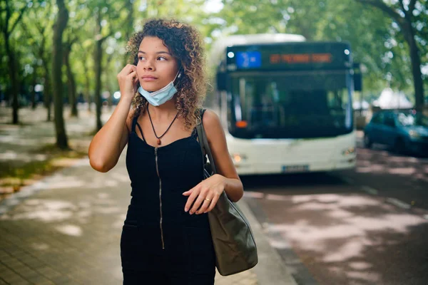 Woman wearing face mask at the bus station with a bus behind her