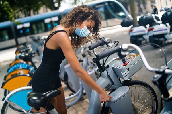 Girl wearing mask take bicycle from rental bike station in the city