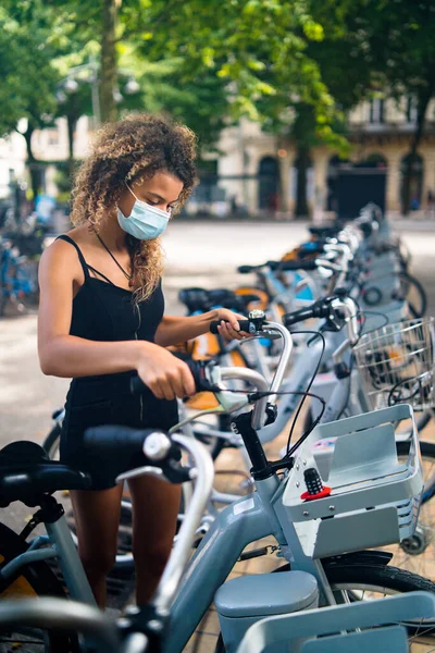 Young woman wearing mask against coronavirus using city rental bicycles