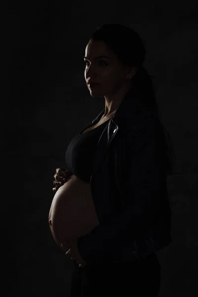 Fechar a barriga da grávida, vista lateral. silhueta de mulher grávida em um fundo preto — Fotografia de Stock