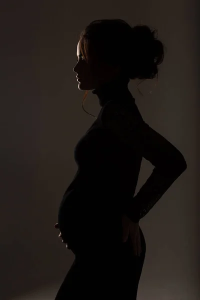 Fechar a barriga da grávida, vista lateral. silhueta de mulher grávida em um fundo preto — Fotografia de Stock