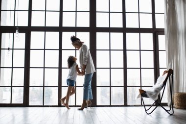 Mutlu sevgi dolu afro Amerikan aile. Genç anne ve çocuk odasında oynarken onun kızı. Anne ve kızı büyük bir pencere arka plan üzerinde dans ediyor
