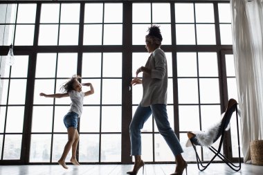 Mutlu sevgi dolu afro Amerikan aile. Genç anne ve çocuk odasında oynarken onun kızı. Anne ve kızı büyük bir pencere arka plan üzerinde dans ediyor