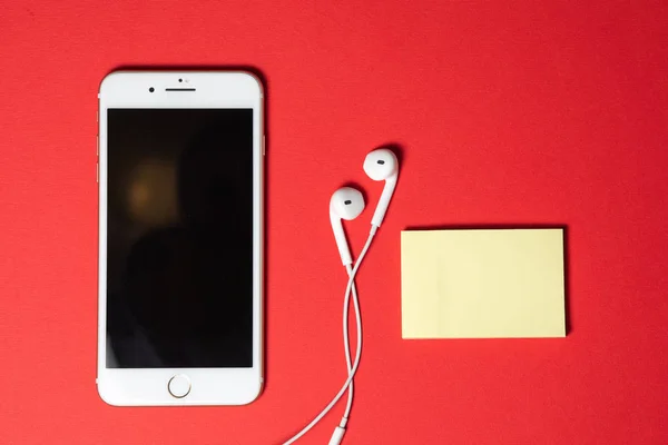 Smartphone com tela em branco se conecta a fones de ouvido com cabo espiral na vista superior de fundo vermelho — Fotografia de Stock