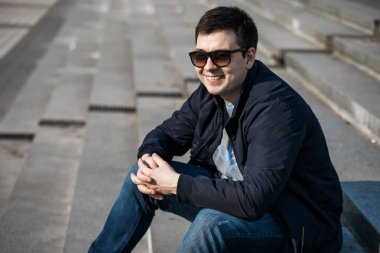 Genç bir adam şehirde kahve içer ve dışarıda yürür..