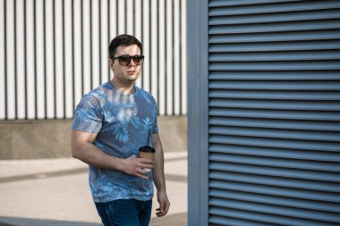 Genç bir adam şehirde kahve içer ve dışarıda yürür..