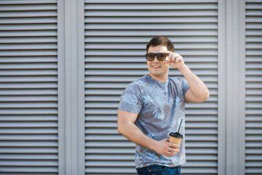 Genç bir adam şehirde kahve içer ve dışarıda yürür..