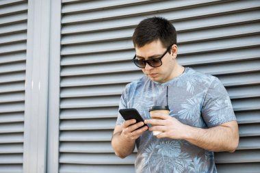 Genç adam şehirde kahve içiyor ve bir mobil içine bakıyor 