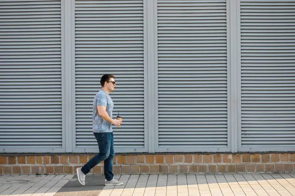 A young man drinks coffee in the city and walks outside.