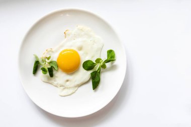 Beyaz tabakta yeşil salata ile kızarmış yumurta. Beyaz arka planda yalıtılmış