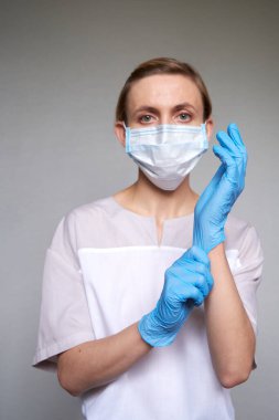 Gri arka planda koruyucu tıbbi maskeli kadın doktor ya da bilim adamına yakın durun. Eldiven takıyor.