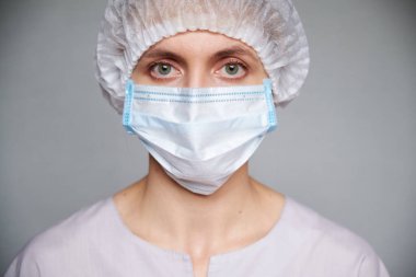 Gri arkaplan üzerinde tıbbi maskesi ve cerrahi kapağı olan kadın doktor ya da bilim adamına yakın çekim.