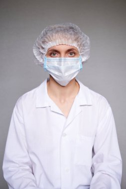 Gri arkaplan üzerinde tıbbi maskesi ve cerrahi kapağı olan kadın doktor ya da bilim adamına yakın çekim.