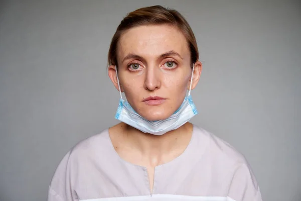 Gri arka planda koruyucu maske takan kadın doktor ya da bilim adamına yakın durun. Tıbbi maske çeneye kadar indirilir.