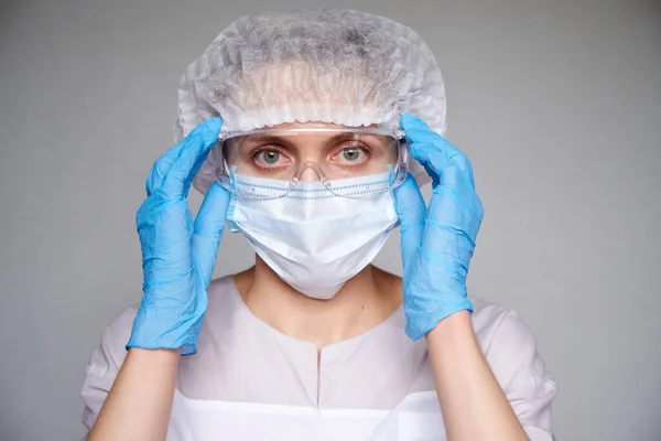 Tıbbi maskeli, cerrahi şapkalı, gözlüklü ve eldivenli kadın doktor ve bilim adamlarına yakın plan gri arka plan.