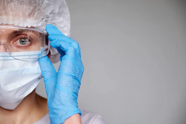 Tıbbi maskeli, cerrahi şapkalı, gözlüklü ve eldivenli kadın doktor ve bilim adamlarına yakın plan gri arka plan.