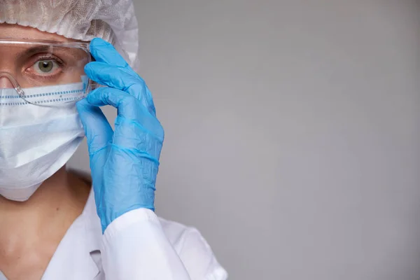 Tıbbi maskeli, cerrahi şapkalı, gözlüklü ve eldivenli kadın doktor ve bilim adamlarına yakın plan gri arka plan.
