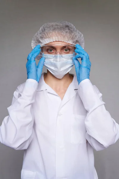 Tıbbi maskeli, cerrahi şapkalı, gözlüklü ve eldivenli kadın doktor ve bilim adamlarına yakın plan gri arka plan.