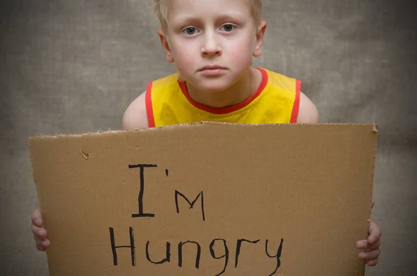 En hungrig pojke i en gul T-shirt med en kartong tablett med inskriptionen jag är hungrig. Det sociala problemet. — Stockfoto