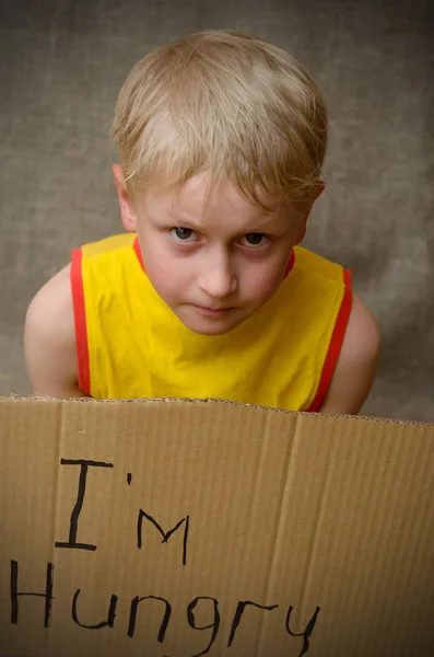 En hungrig pojke i en gul T-shirt med en kartong tablett med inskriptionen jag är hungrig. Det sociala problemet. — Stockfoto