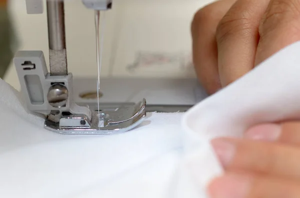 Seamstresses dikiş makinesi arkasında beyaz malzeme ile eller.