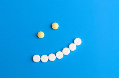 Mavi zemin üzerine beyaz ve sarı haplardan gülümseme.