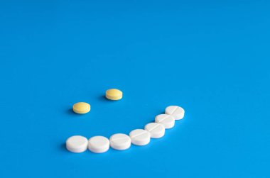 Mavi zemin üzerine beyaz ve sarı haplardan gülümseme.