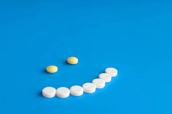 Mavi zemin üzerine beyaz ve sarı haplardan gülümseme.
