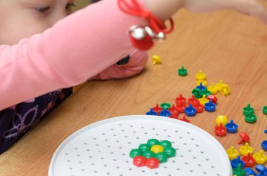 Küçük bir kız masada renkli mozaik toplar.