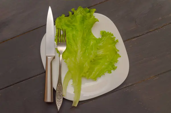 Листя салату на білій тарілці з виделкою та ножем. Сірий дерев'яний фон. Концепція здорового харчування . — стокове фото