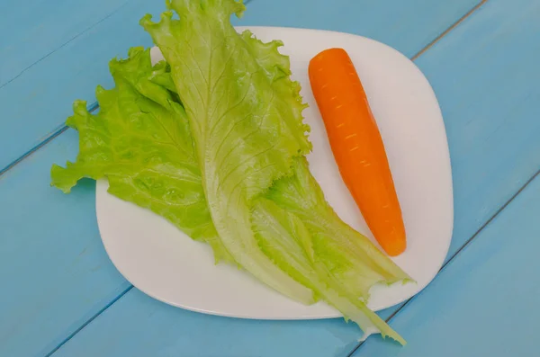 Lechuga con zanahoria en un plato blanco. Fondo azul madera. El concepto de alimentación saludable . — Foto de Stock