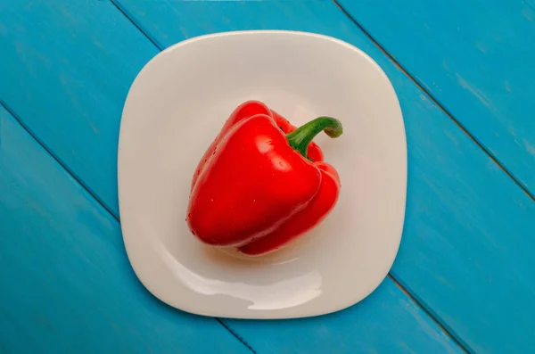 Bulgarian red pepper on a white plate. Wooden blue background. The concept of healthy eating. — Stock Photo, Image