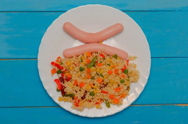 Placa blanca con dos salchichas y arroz con verduras sobre fondo de madera azul . — Foto de Stock